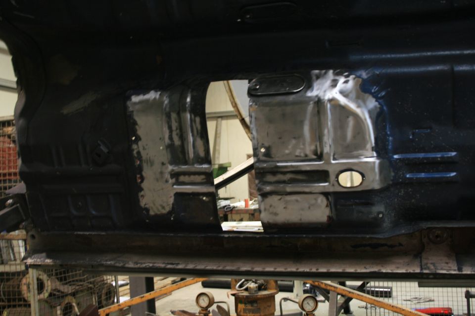 Underside of a vehicle with metal patches on the floor pan, possibly undergoing repair