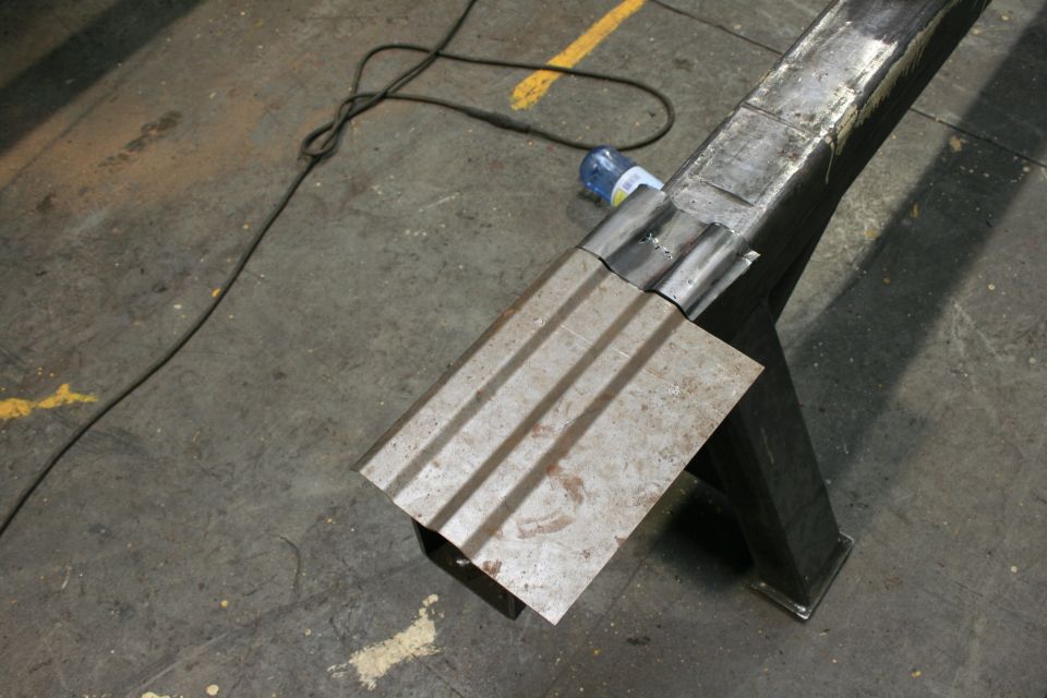 Metal sheet being welded to a frame, with a power cord and bottle on the floor
