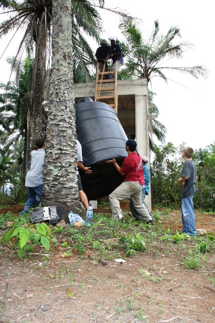 1987 Ford Bronco - A group of people work together to maneuver a large water tank into place near a building.