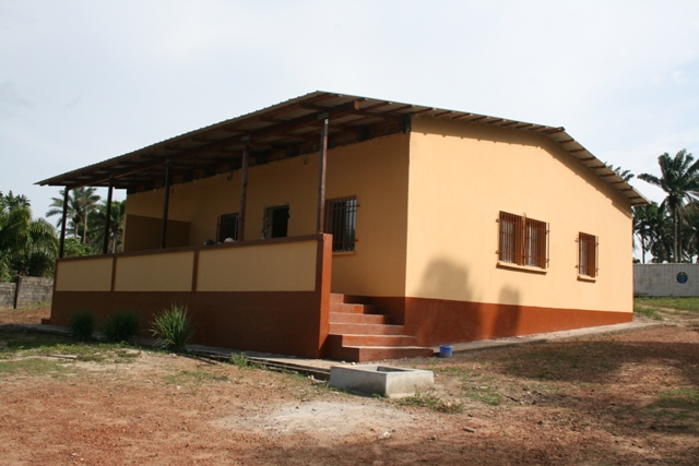 building with tan walls, brown trim, and a corrugated metal roof with a covered porch