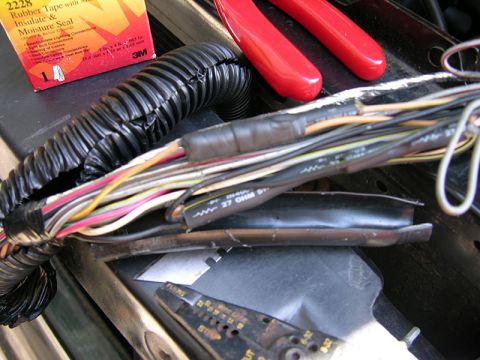 1990 Ford Bronco - Close-up of a vehicle's wiring harness with tools and tape, suggesting automotive repair work.