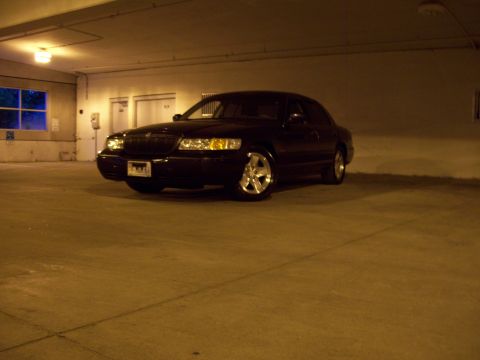 1999 Mercury Grand Marquis - A dark sedan with custom wheels sits in a concrete parking structure.