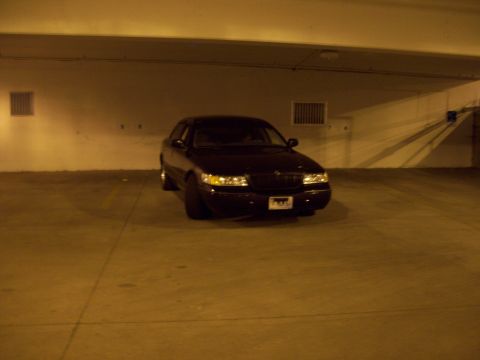 1999 Mercury Grand Marquis - A dark sedan is parked in a dimly lit garage with its headlights on.