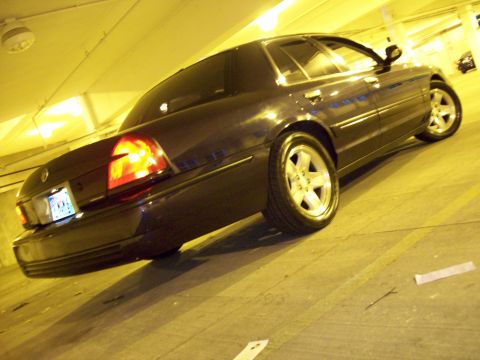 1999 Mercury Grand Marquis - Rear view of a dark sedan with aftermarket wheels in a parking garage.