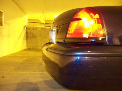 1999 Mercury Grand Marquis - The taillight of a dark sedan is illuminated, parked in a dimly lit garage with yellow walls.