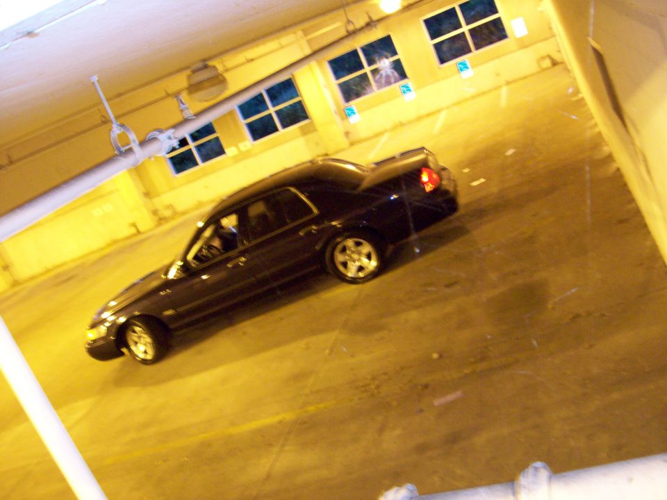 Dark sedan parked in a dimly lit indoor area with yellow walls and windows