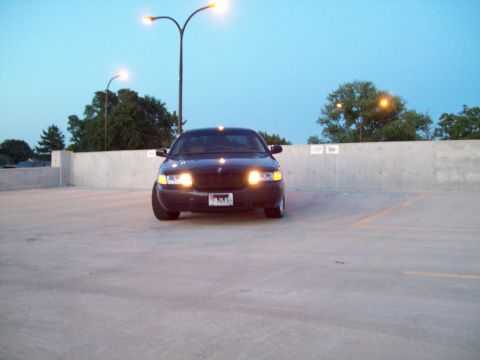 1999 Mercury Grand Marquis - This black sedan, likely a 2003 model, is parked in an outdoor lot with its headlights illuminated.