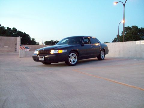 1999 Mercury Grand Marquis - A dark 1999 Mercury Grand Marquis is parked on a concrete surface under a dusky sky.