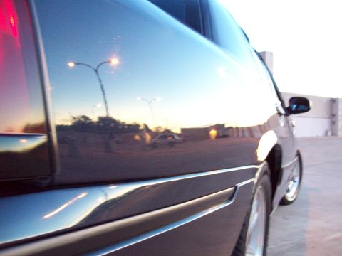 1999 Mercury Grand Marquis - A dark sedan is captured in a 3/4 front view, with the polished body reflecting the surrounding environment and streetlights.