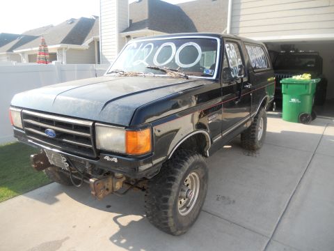 1991 Ford Bronco - A black Ford Bronco is parked in a driveway with a "For Sale" sign on the window.
