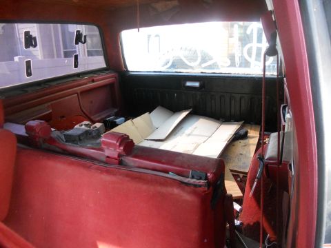 1991 Ford Bronco - The interior of a vehicle shows a red seat and debris in the cargo area, with a view of the outside through the rear window.