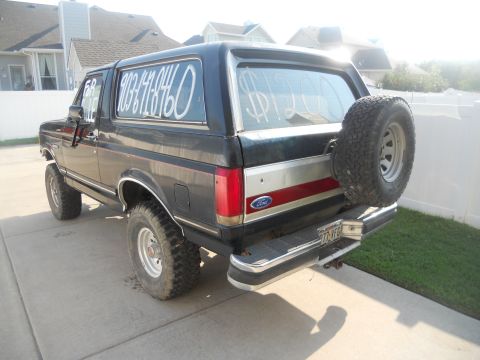 1991 Ford Bronco - Rear view of a black Ford Bronco with a spare tire mounted on the tailgate and a phone number on the window.