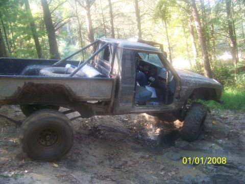 1989 Ford Bronco - Off-road pickup truck with a roll cage navigates a muddy trail.