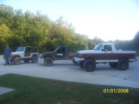 1989 Ford Bronco - A modified pickup truck tows a Jeep, with another Jeep and a man standing nearby.