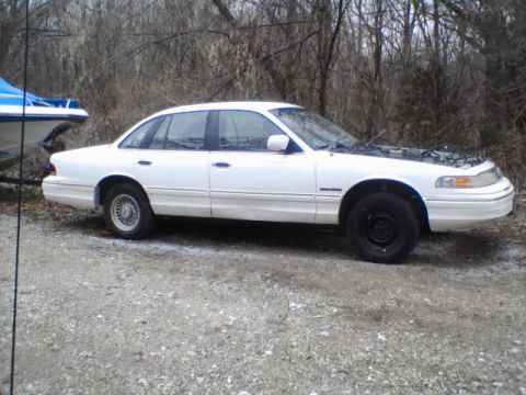 1994 Ford Crown Victoria - A white 1994 Ford Crown Victoria is parked outdoors with its hood up, next to a boat on a trailer.