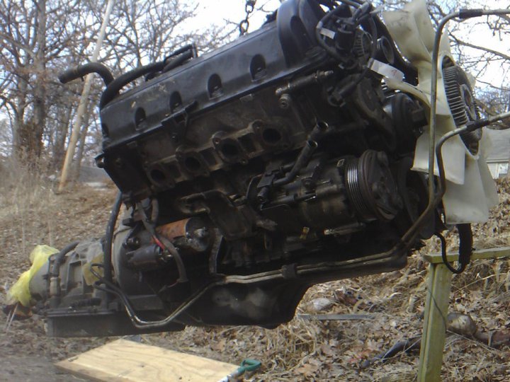 Engine and transmission assembly suspended by a chain, with a fan visible