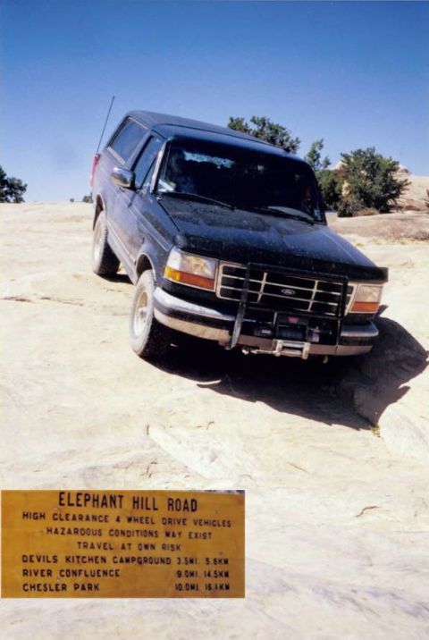 1995 Ford Bronco - This dark-colored Ford Bronco is parked on a rocky, off-road trail under a clear blue sky.