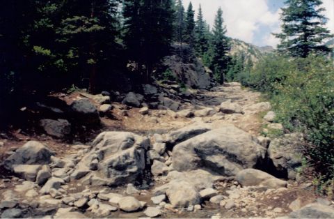 1995 Ford Bronco - A mountain trail winds through boulders and pine trees under a partly cloudy sky.