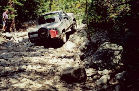 1995 Ford Bronco - A person watches a Ford Bronco navigate a difficult, rocky path through a wooded area.
