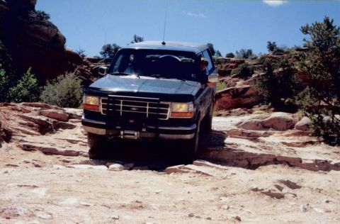 1995 Ford Bronco - Ford Bronco tackles a challenging off-road path under a clear blue sky.
