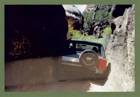 1995 Ford Bronco - A 1995 Ford Bronco navigates a dusty trail surrounded by canyon walls.