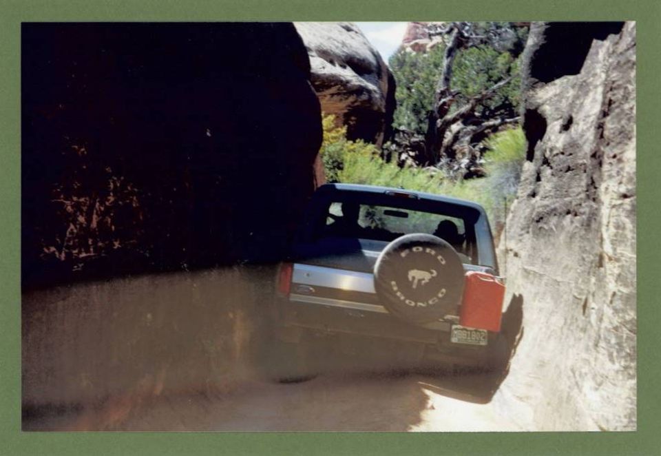 Ford Bronco with spare tire on back driving through a narrow canyon