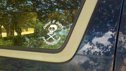 1995 Ford Bronco - A sticker with a skull and crossed wrenches is affixed to the window of a dark-colored vehicle.