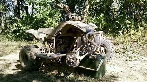 1995 Ford F-150 - A muddy quad bike sits in a wooded area, its front end elevated slightly.