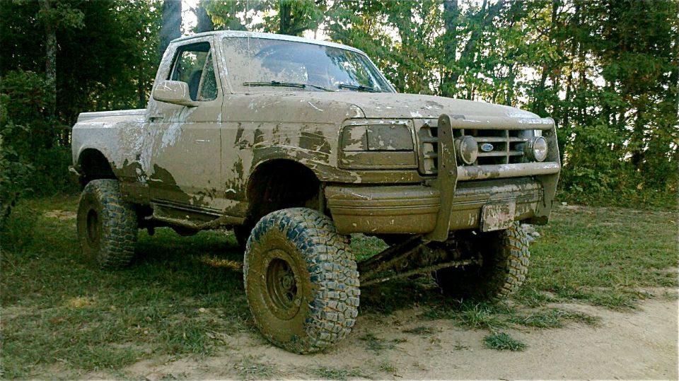 Muddy pickup truck with lifted suspension and large tires parked in a grassy area