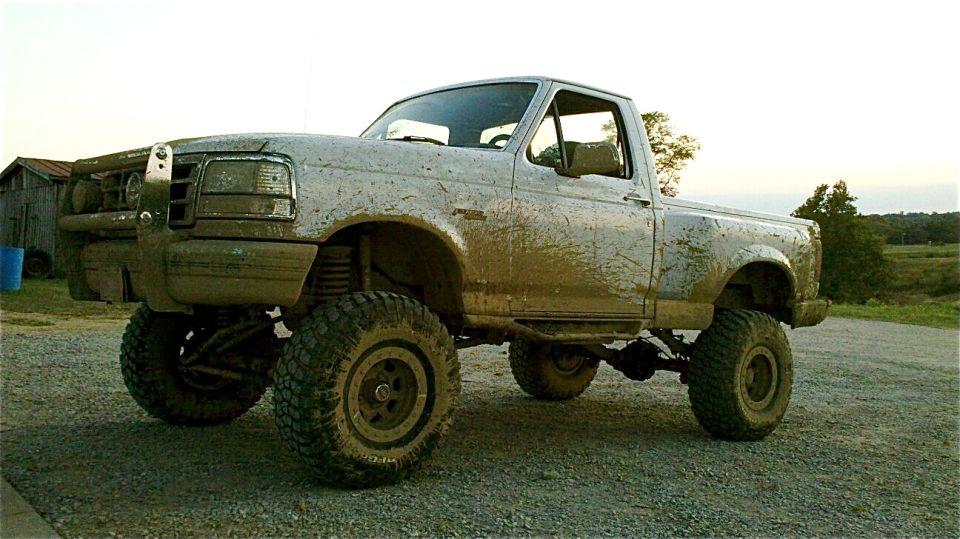 Mud-covered white Ford F-150 pickup truck with lifted suspension and large tires
