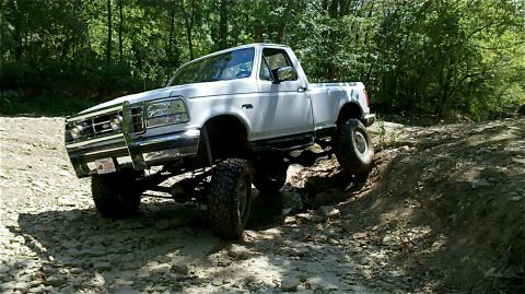 1995 Ford F-150 - This lifted pickup truck navigates a challenging off-road trail with trees in the background.