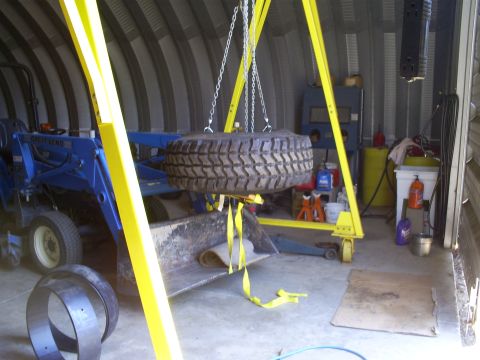 1992 Ford Bronco - A blue tractor sits in a garage, with a large tire being held by a yellow gantry above its front loader.