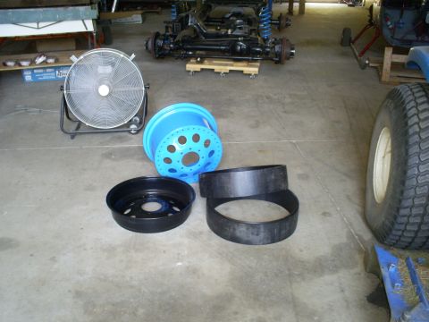 1992 Ford Bronco - Vehicle chassis and various parts, including a fan, blue wheel, and tire components, are laid out on a concrete floor.