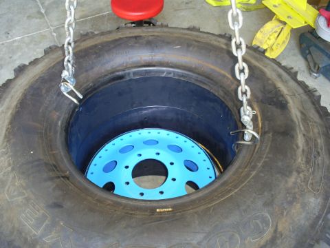 1992 Ford Bronco - A large tire is shown with a blue wheel inside, held up by chains.