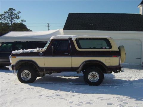 1979 Ford Bronco - This two-tone 1979 Ford Bronco is parked in the snow, showing its side profile with a spare tire mounted on the rear.