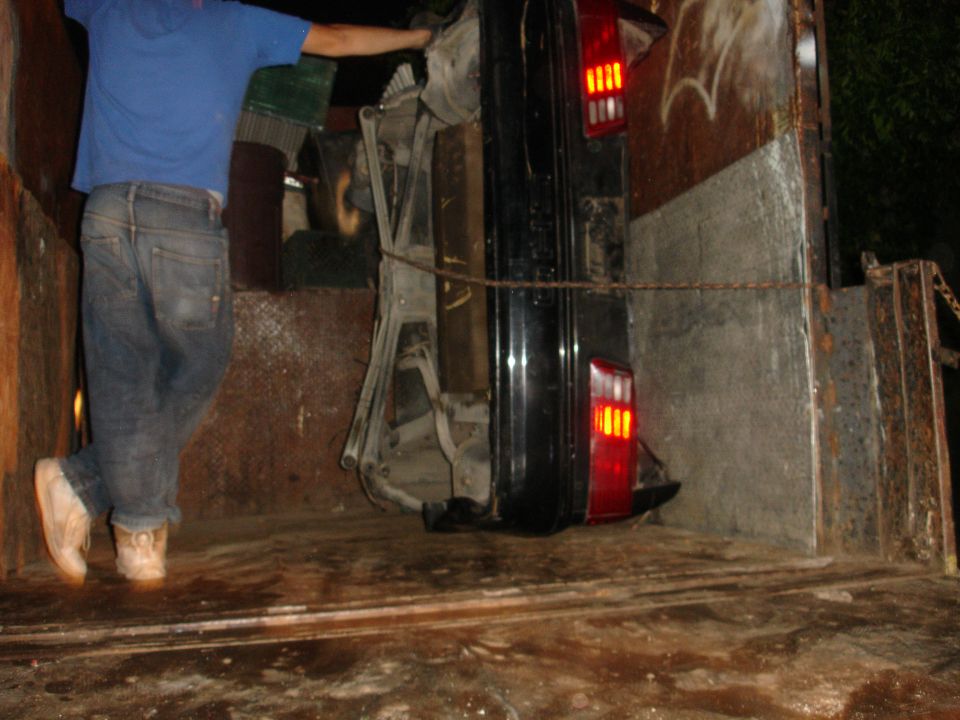 Black 1989 Ford Taurus, upside down and chained in a truck bed, rear view showing taillights