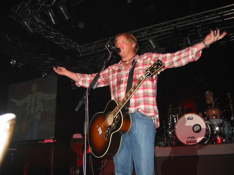 Musician with acoustic guitar and arms outstretched on a concert stage
