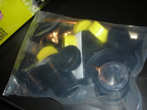 1998 Ford Crown Victoria - clear bag of yellow and black polyurethane bushings and brass sleeves sits next to a yellow label reading WORLD'S, on a dark surface.