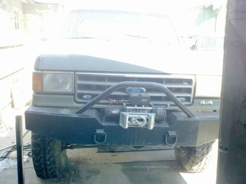 1989 Ford Bronco - Front view of a green Ford Bronco with a custom bumper and winch, showing its grille and 4x4 badging.