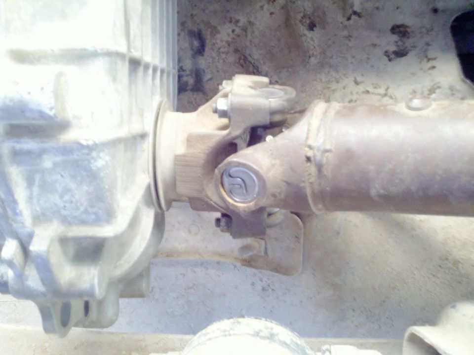 Close-up of a driveshaft connected to a transfer case, showing U-joints and yokes