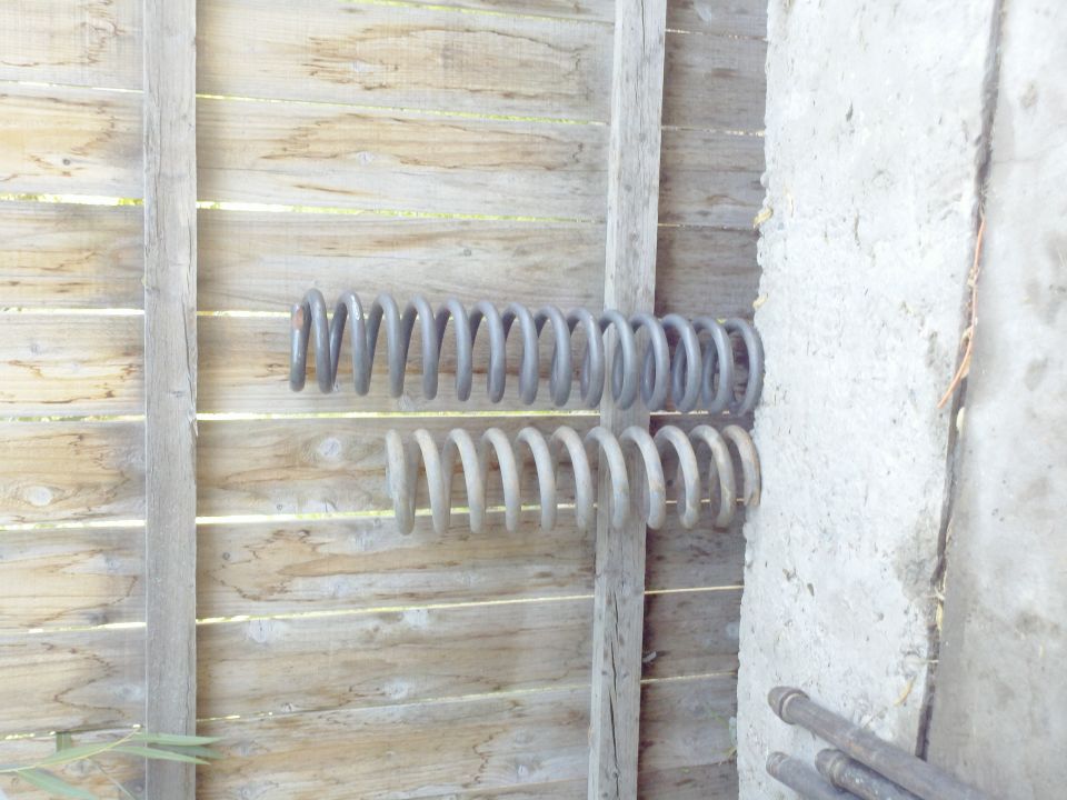 Two suspension springs, one larger and darker than the other, mounted on a wooden fence