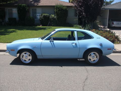 1972 Ford Pinto - A light blue 1972 Ford Pinto coupe is parked on the side of a street in front of a house.