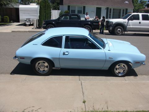 1972 Ford Pinto - A light blue 1970s hatchback car is parked on a suburban street next to other vehicles.
