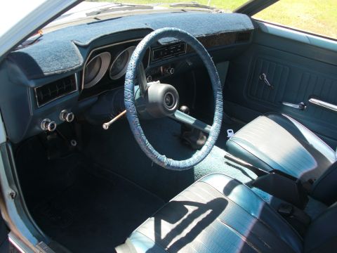 1972 Ford Pinto - The interior of a 1972 Ford Pinto shows blue vinyl seats and a dashboard with a blue steering wheel cover.