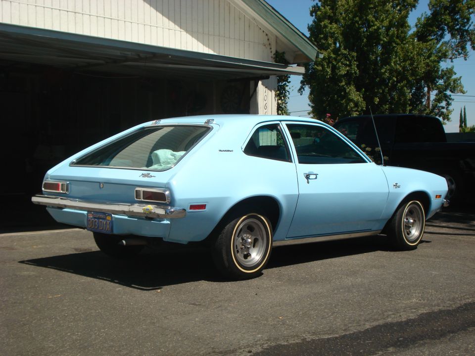 Light blue 1972 Ford Pinto hatchback parked in front of a garage, rear quarter view