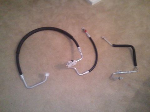 1994 Ford Bronco - Two automotive AC hoses and a metal tube assembly are laid out on a carpeted floor.