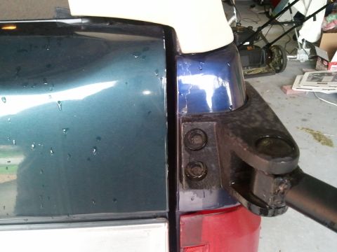 1994 Ford Bronco - This image shows a close-up of the rear corner of a blue SUV, with visible water droplets on the paint and a black bracket attached.