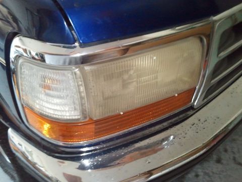 1994 Ford Bronco - Close-up of a blue Ford Bronco's front corner, showing the headlight and chrome bumper details.