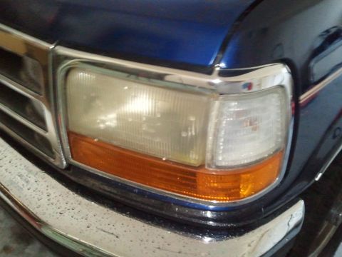 1994 Ford Bronco - Close-up of the front corner of a blue 1994 Ford Bronco, highlighting the headlight and chrome grille.