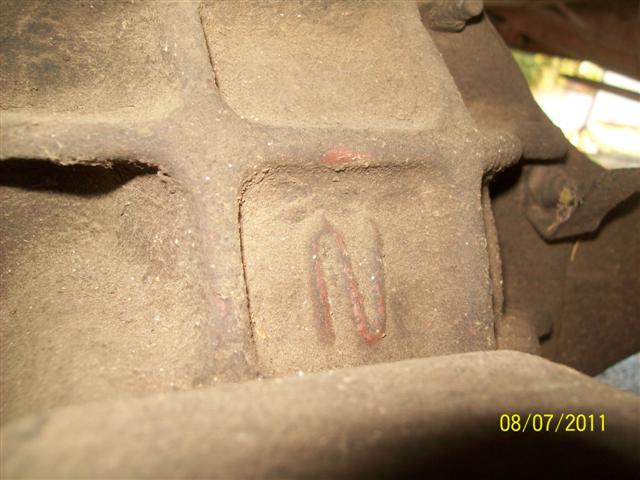 Close-up of cast letter N marked in red paint on a dirty cast iron housing under a 1979 Ford F-150